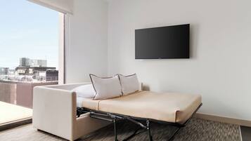 Una moderna camera d'hotel con un letto, una TV a parete e vista sulla città attraverso la finestra.