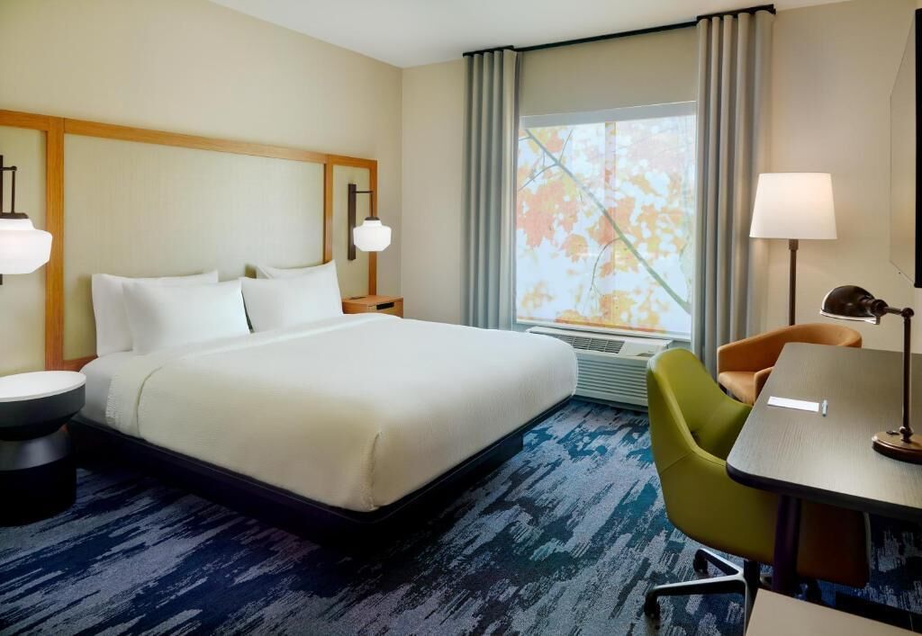 A hotel room with a large bed, a desk, a chair, a lamp, and a window with curtains.