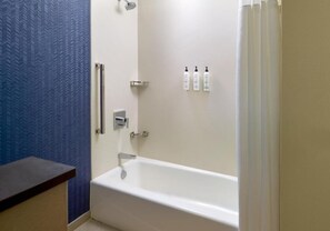 A bathroom with a white bathtub, a shower, and a blue textured wall. There are three bottles of toiletries on the wall. - Fairfield By Marriott Inn & Suites Savannah Pooler (Pooler)