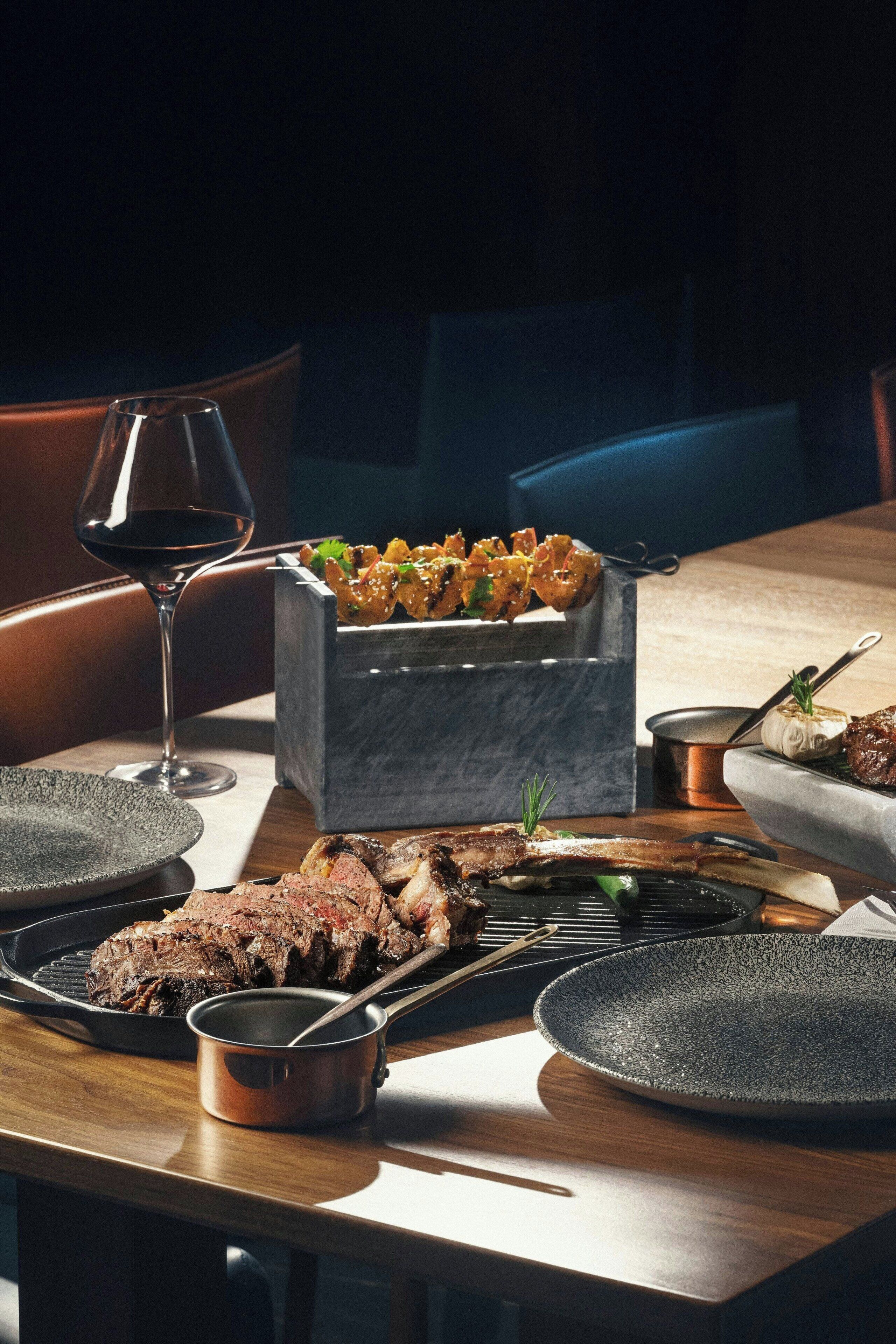 Een eettafel met een steak, een wijnglas en een metalen bak met eten.