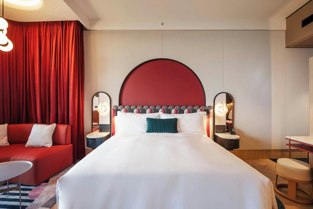Una habitación de hotel con una cama grande, un sofá rojo, un escritorio y un espejo.