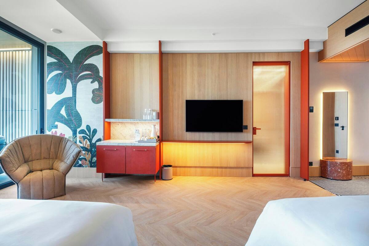 Habitación de hotel moderna con una cama grande, un escritorio con televisor de pantalla plana, una silla y un mural decorativo en la pared.