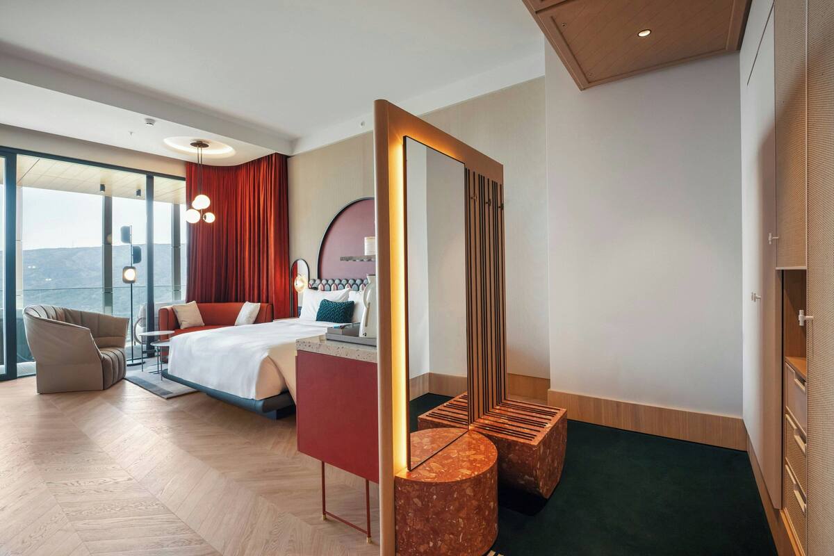 Habitación de hotel moderna con una cama grande, zona de estar, un espejo amplio y vistas a la ciudad.
