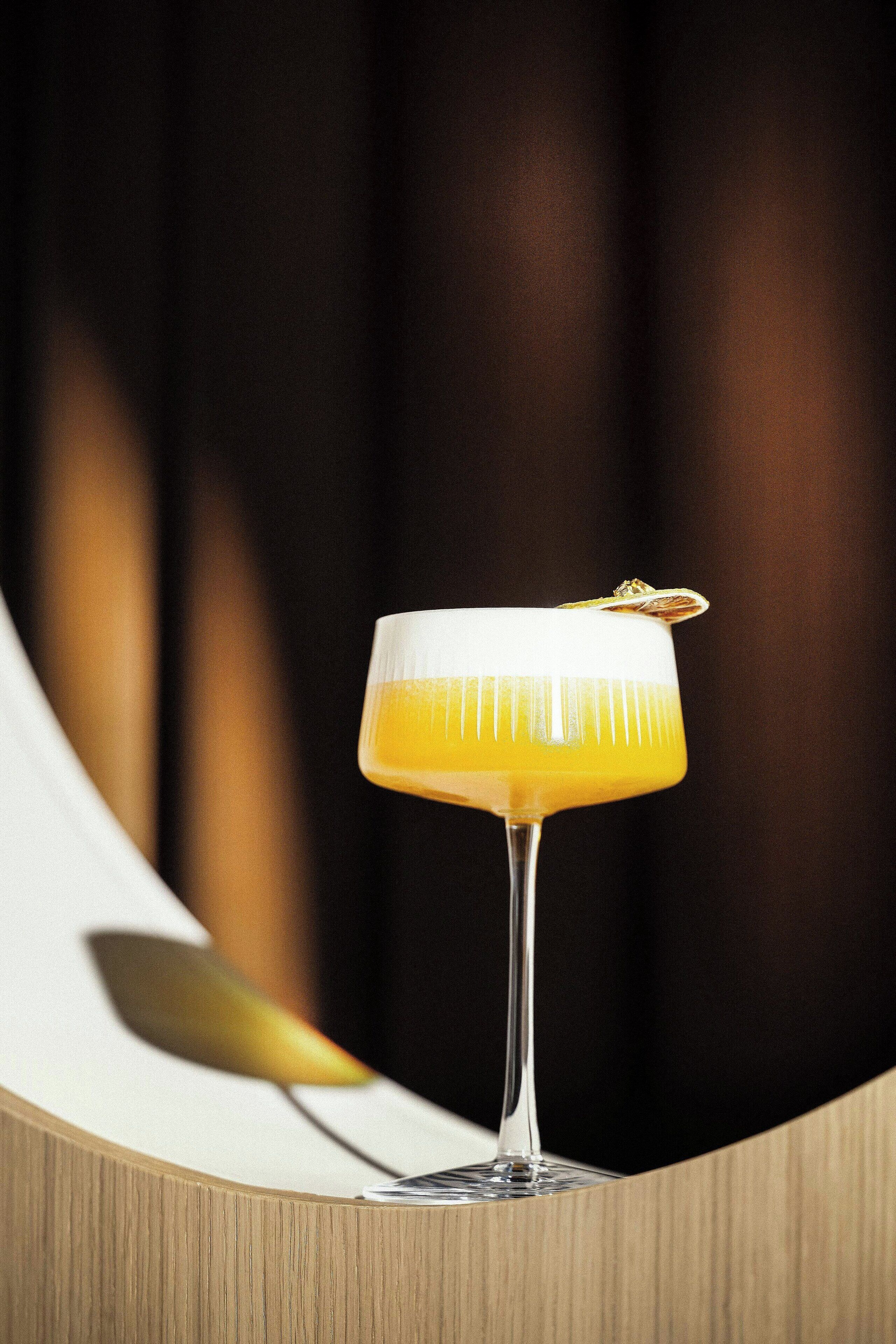 A cocktail in a stemmed glass with a garnish on a wooden surface.