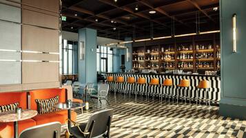A bar area with a patterned floor, seating with orange and black cushions, and shelves stocked with bottles.