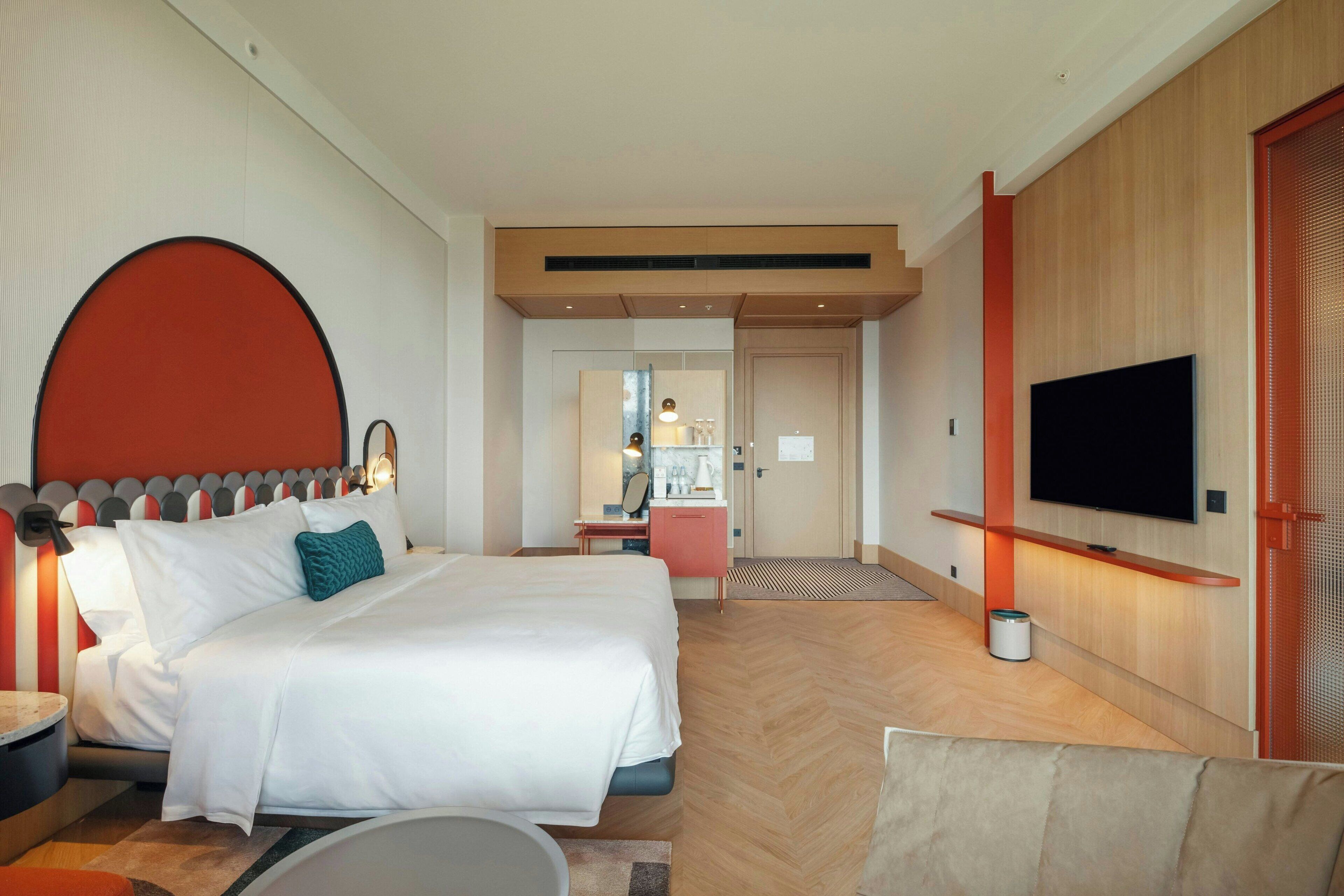 A hotel room with a bed, a TV, a desk, and a bathroom visible in the background.