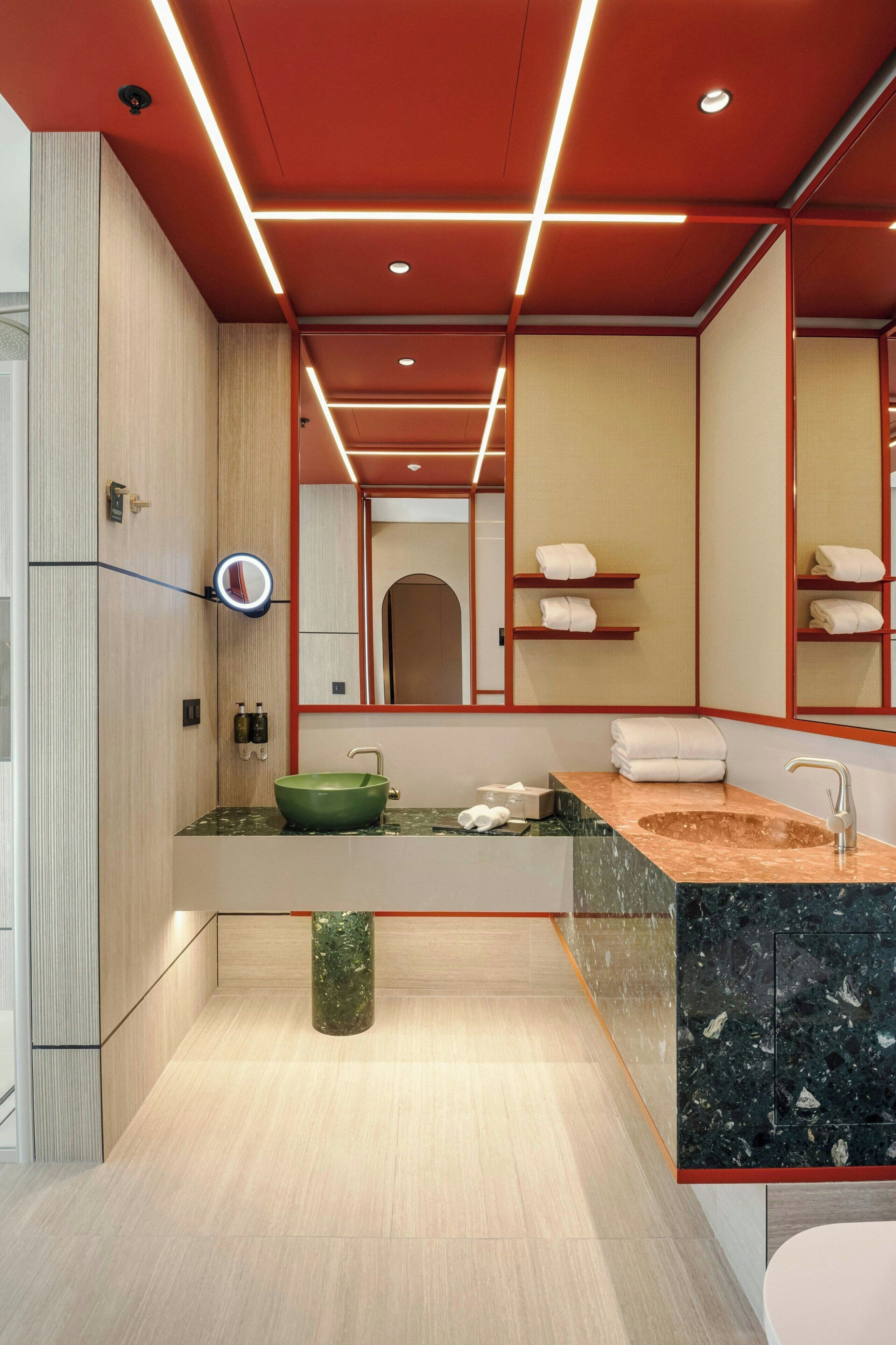 A modern bathroom with a green sink, a mirror, and a red ceiling design.