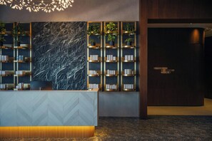 A reception area with a herringbone-patterned desk, a marble wall, and shelves with plants and informational cards.