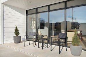 An outdoor seating area with modern chairs and potted plants, a glass wall, and a view of the interior.