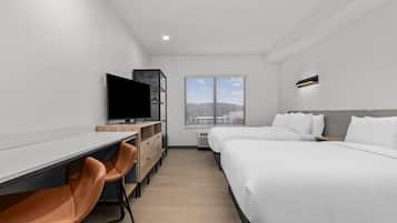 Une chambre d’hôtel moderne équipée d’un bureau, de deux lits, d’une télévision et d’une fenêtre avec des stores.