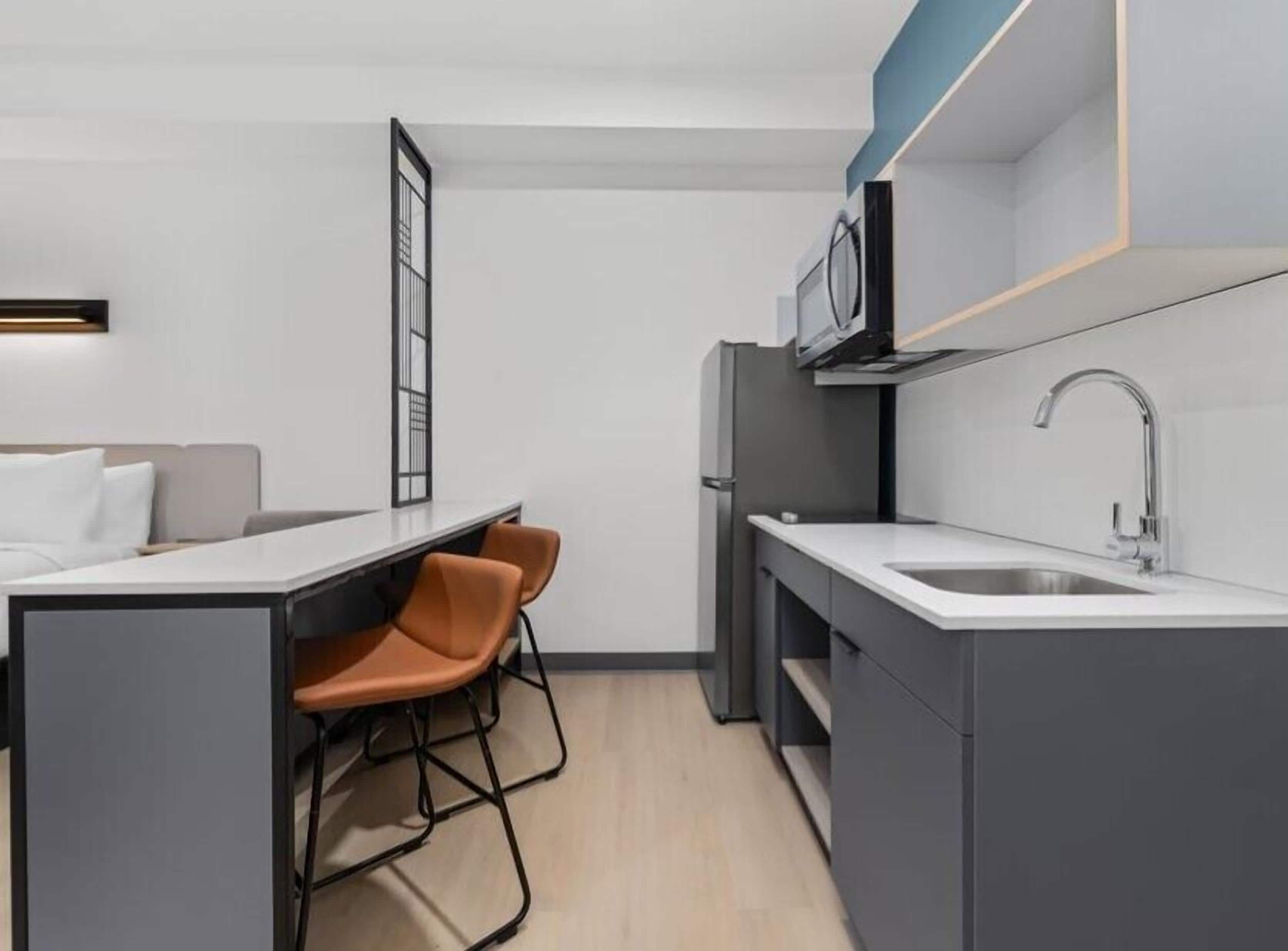 A compact kitchen with a microwave, sink, and a small dining area with chairs.