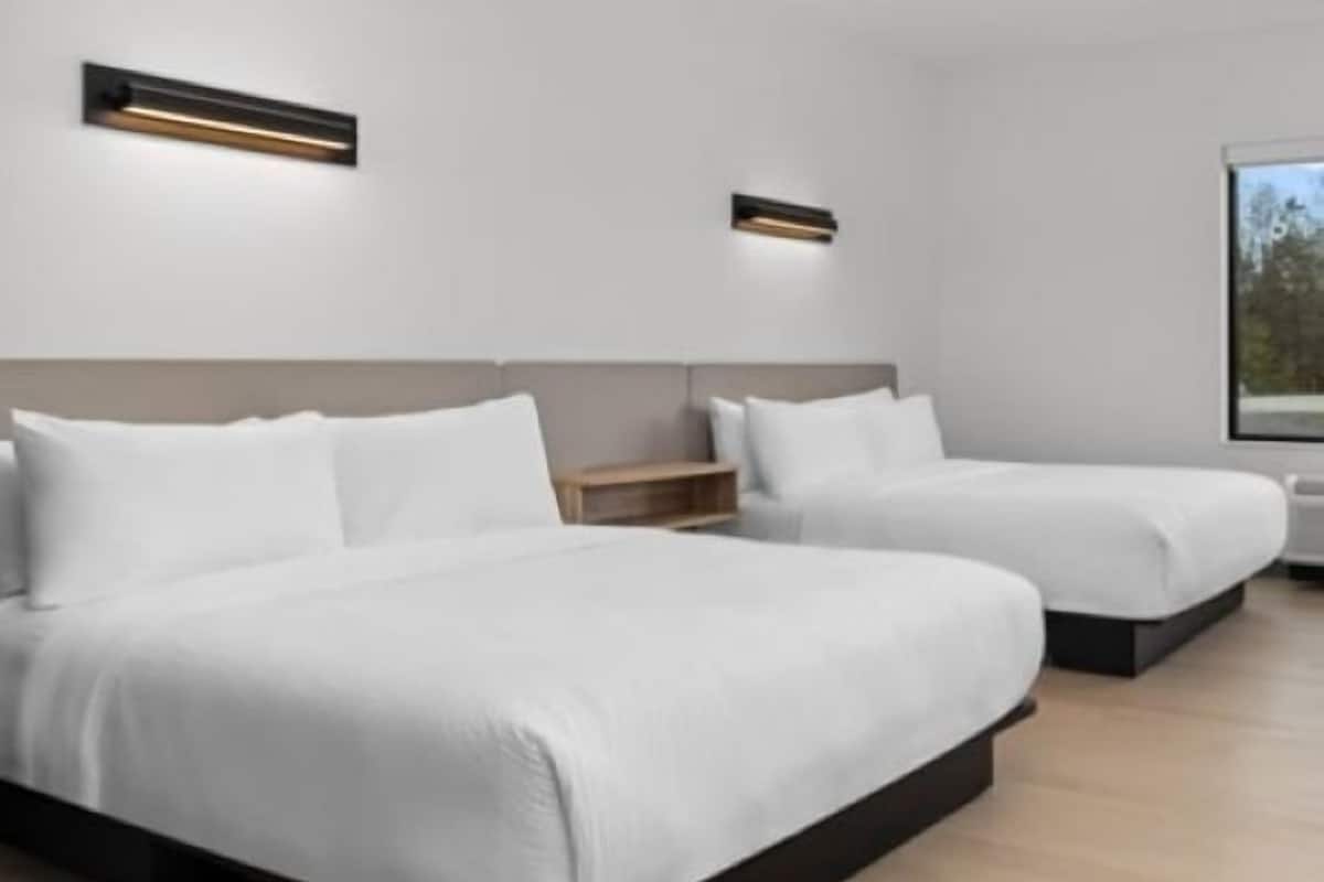 A modern hotel room with two beds, a bedside table, and a large window.