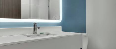 A modern bathroom with a white sink, a mirror, and a toilet.