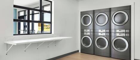 A laundry room with a large window, a white shelf, and six stacked front-loading washing machines.