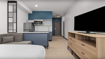 A modern living room with a sofa, a TV on a wooden stand, a kitchen area with a microwave, and a blue accent wall.