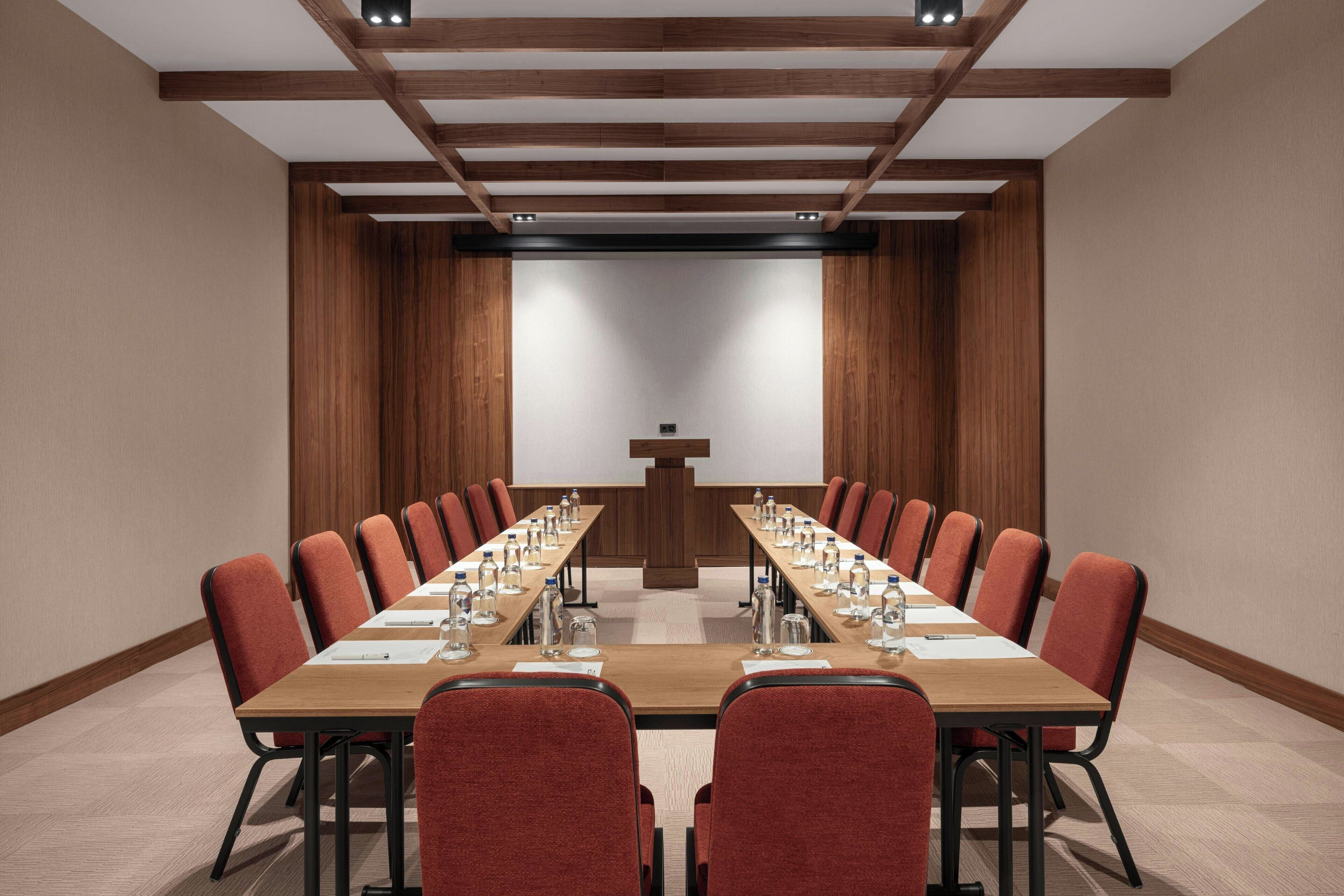 Una sala de conferencias con una larga mesa, sillas rojas y un atril al frente.