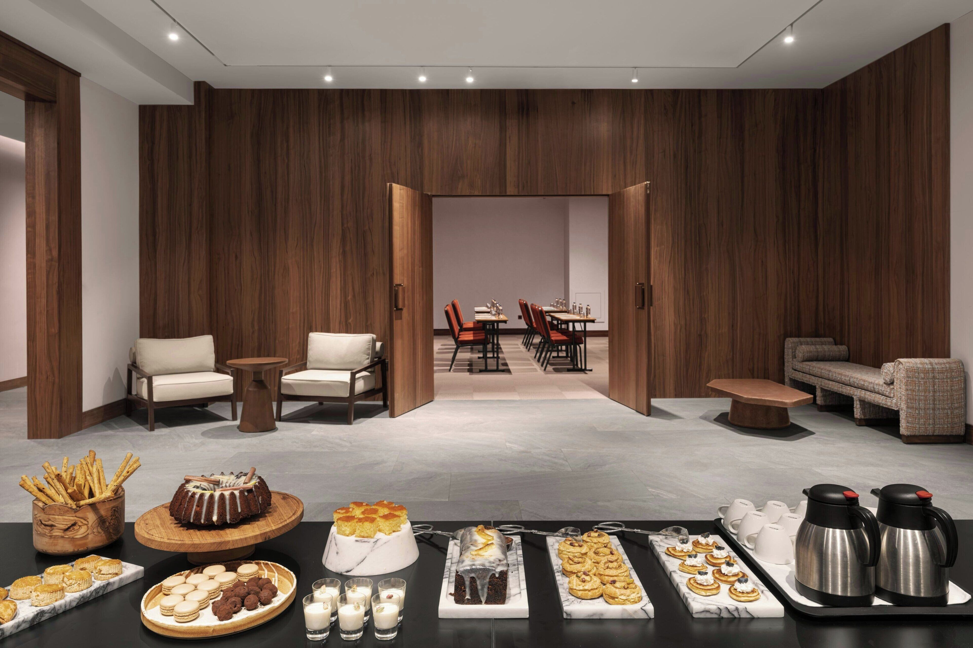 Un moderno hall de hotel con una mesa de buffet, zona de estar y vista hacia un comedor.