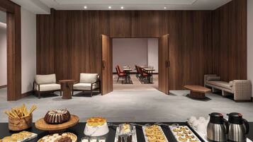 Un moderno hall de hotel con una mesa de buffet, zona de estar y vista hacia un comedor.