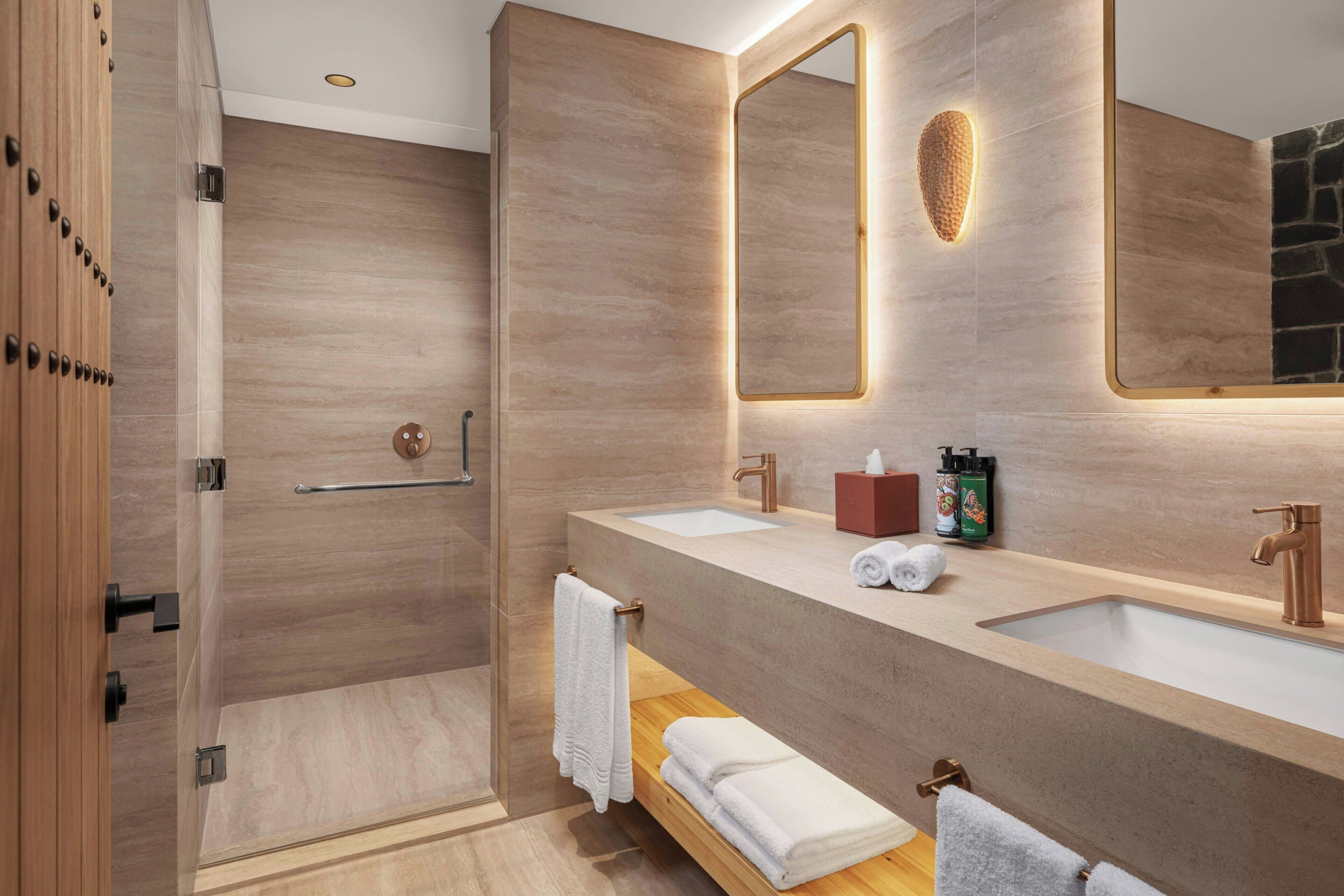 A modern bathroom with two sinks, a large mirror, and a shower area.