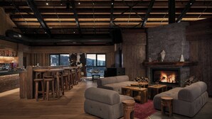Un vaste espace de vie doté d’une cheminée, de canapés, de tabourets de bar en bois et d’une grande fenêtre offrant une vue sur l’extérieur.