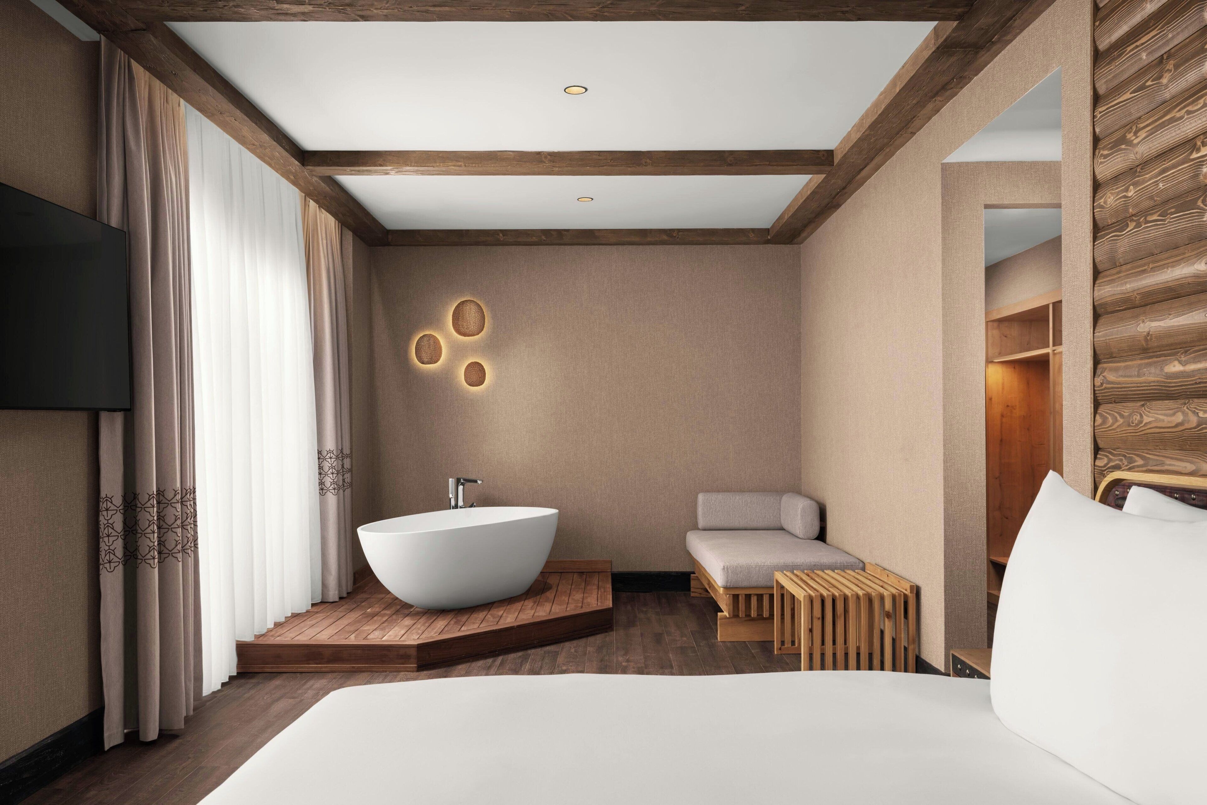 A modern hotel room with a large bed, a freestanding bathtub, a seating area, and a television.