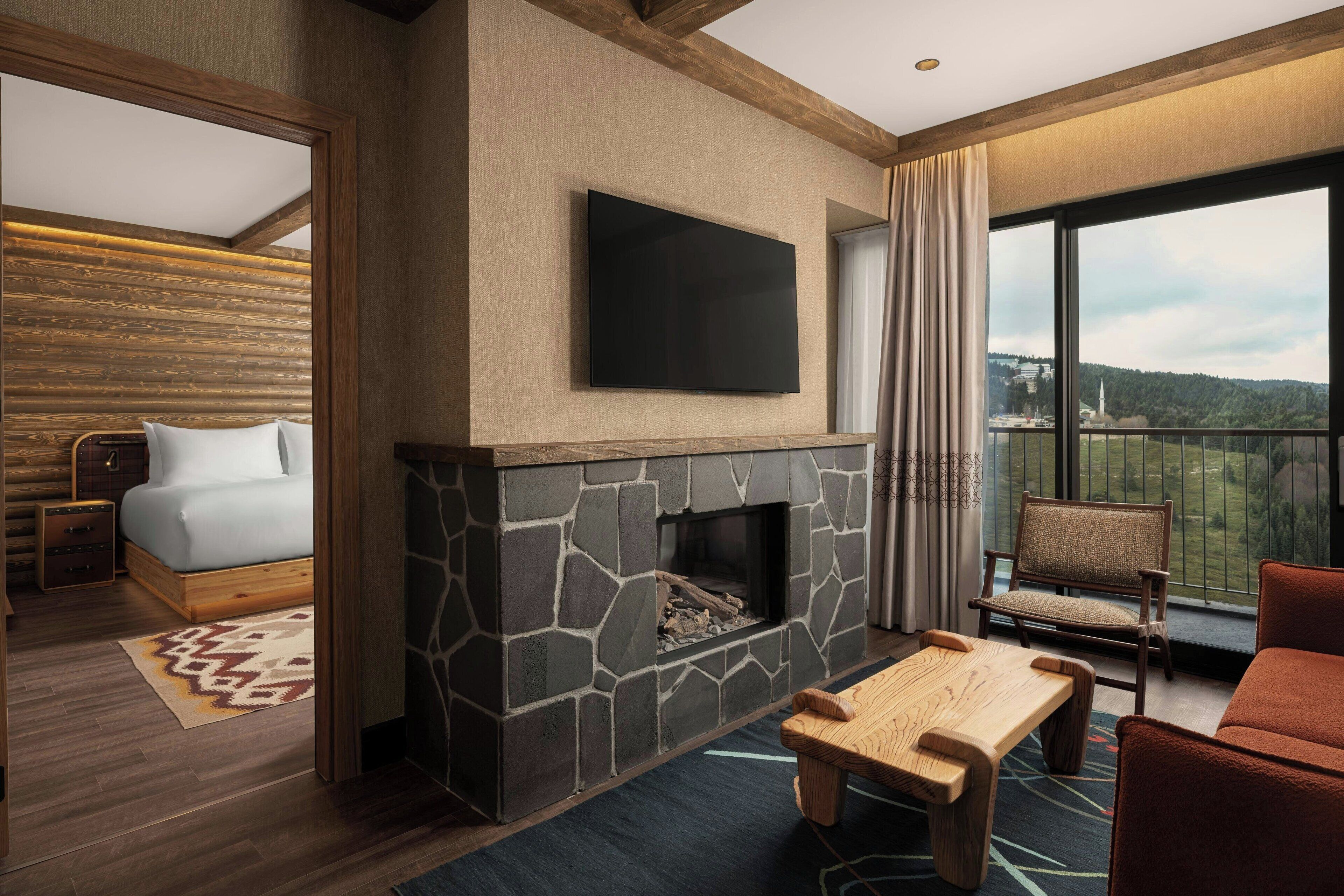 Habitación de hotel moderna con chimenea de piedra, una cama, televisión y balcón con vistas.