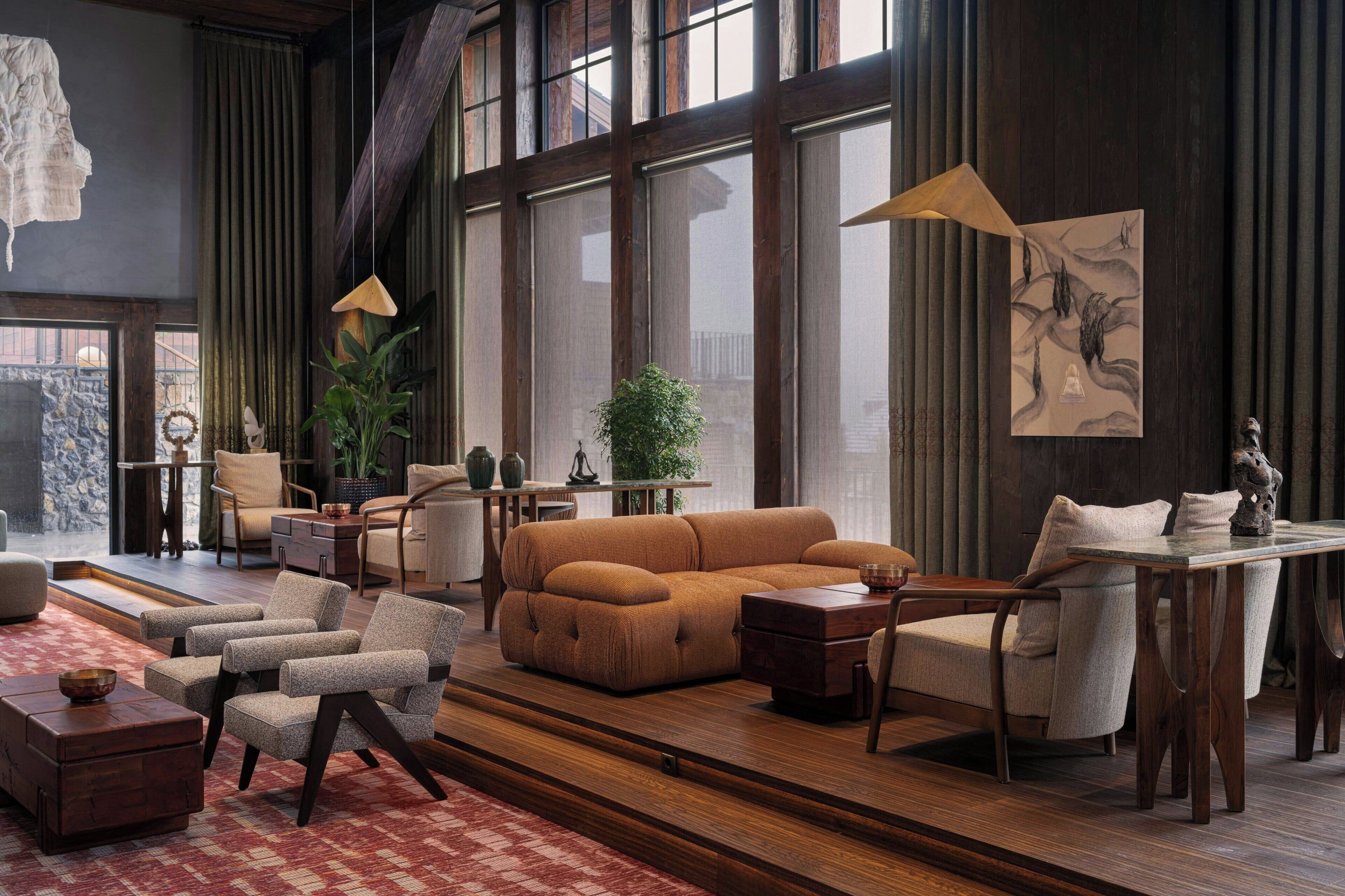 A spacious living room with a large window, a sofa, armchairs, a wooden coffee table, and a dining table with chairs.