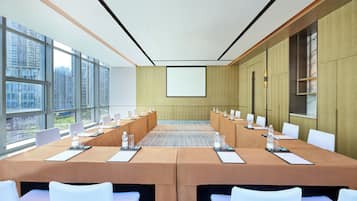 Een vergaderruimte met een lange tafel, witte stoelen en een scherm voor een beamer.
