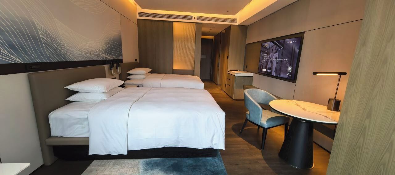 A hotel room with two beds, a desk, a chair, and a TV.