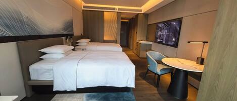 A hotel room with two beds, a desk, a chair, and a TV.