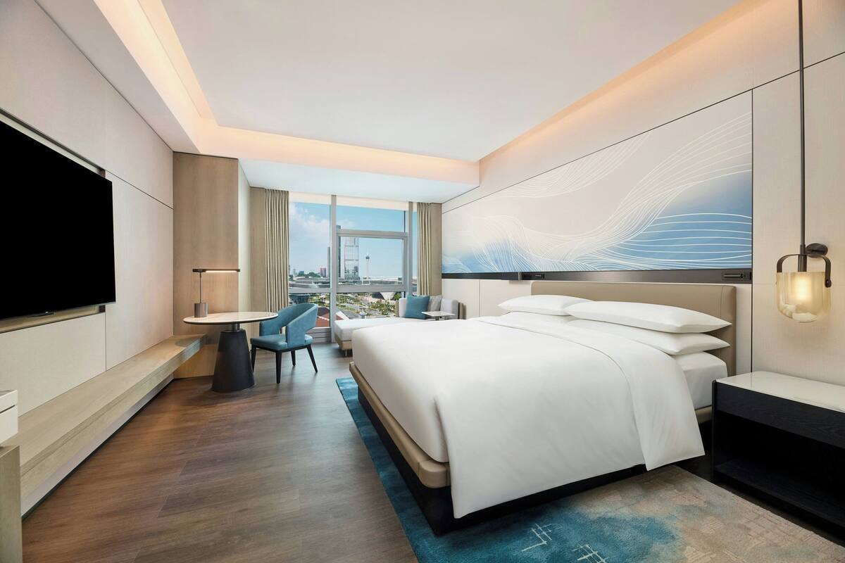 Une chambre d’hôtel moderne dotée d’un grand lit, d’une télévision à écran plat, d’un bureau et offrant une vue sur la ville.