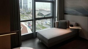 Une chambre d’hôtel moderne dotée d’une grande fenêtre donnant sur la ville, d’un coin salon confortable et d’une table en marbre.