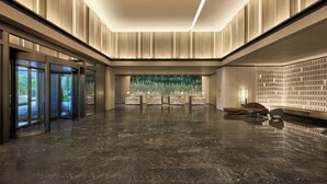 Un lobby amplio con un piso de mármol pulido, un mostrador de recepción y una gran pared decorativa verde.