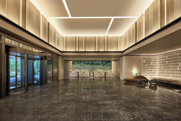 A spacious lobby with a polished marble floor, a reception desk, and a large green wall feature.