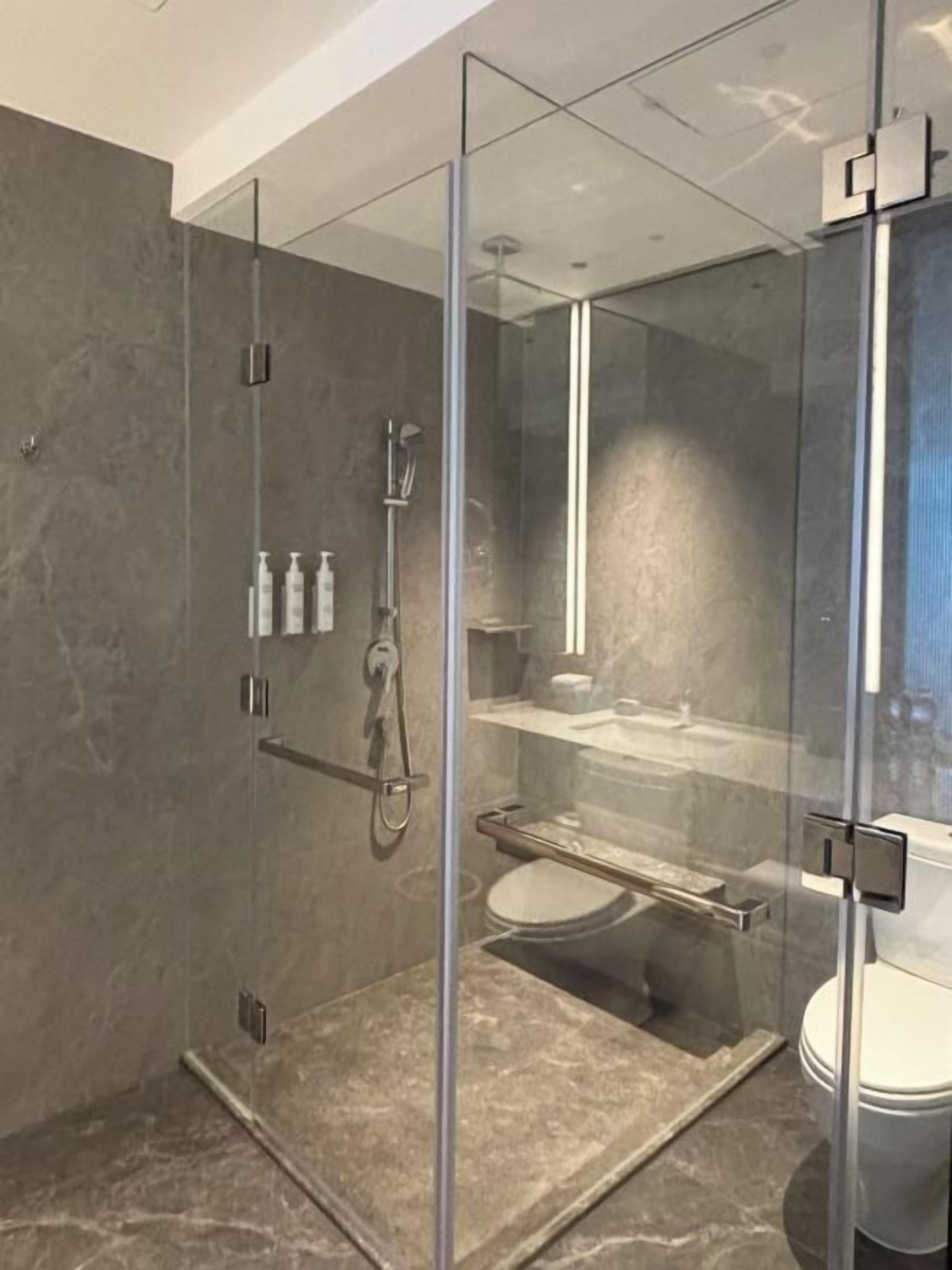 A modern bathroom with a glass-enclosed shower, marble flooring, and a visible toilet.