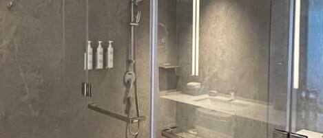 A modern bathroom with a glass-enclosed shower, marble flooring, and a visible toilet.