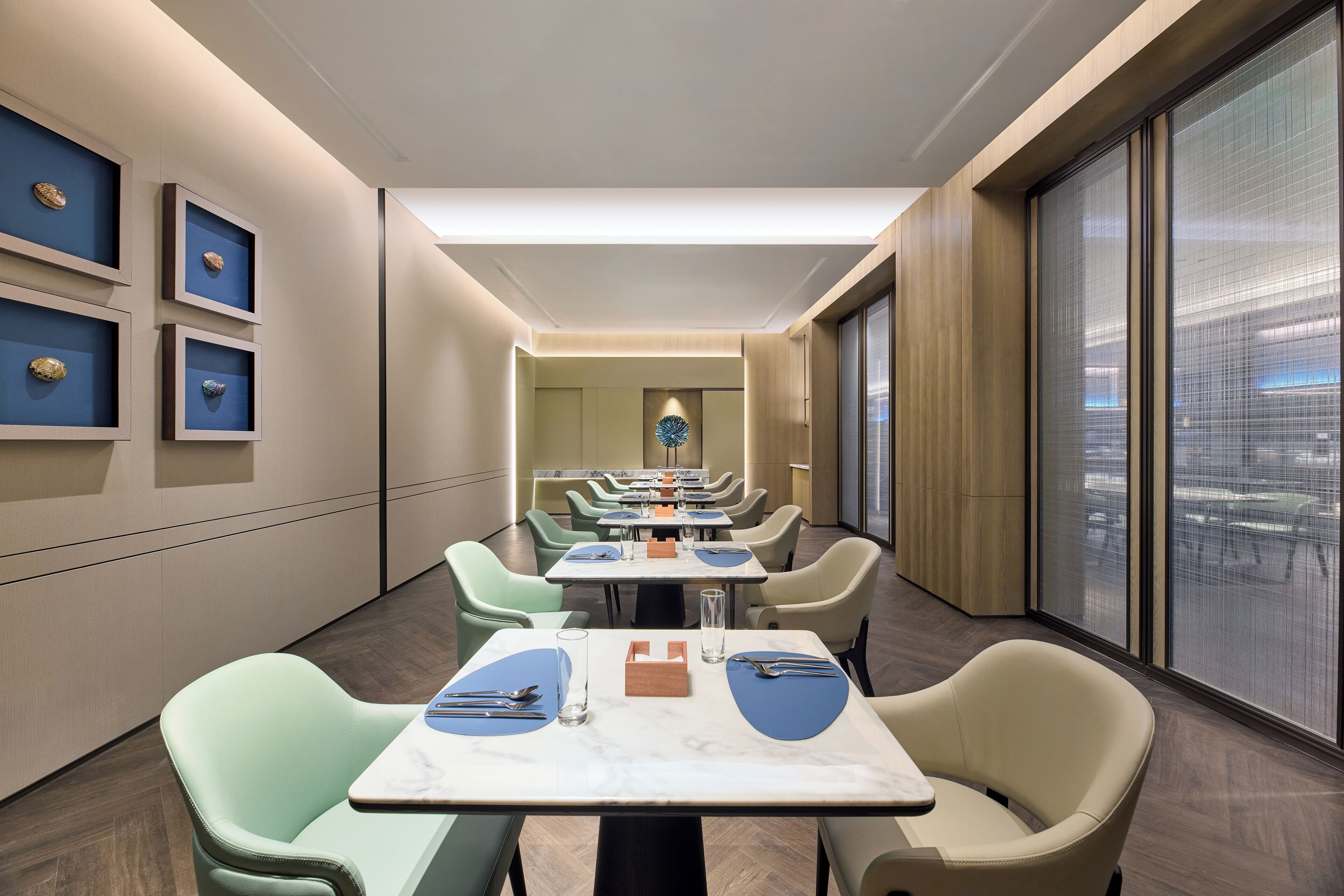 A modern dining area with tables and chairs, framed artwork on the walls, and a view through large windows.