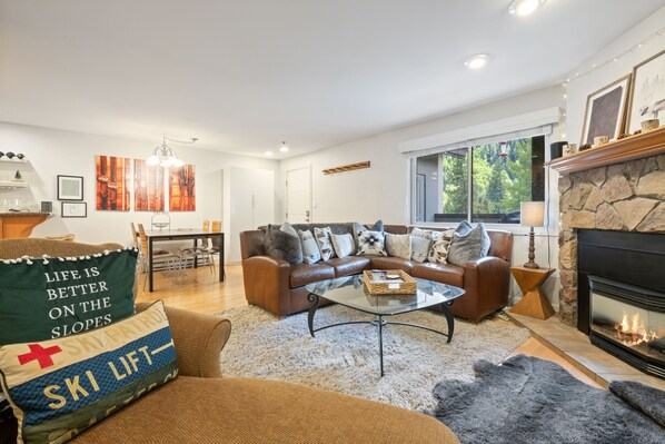 A cozy living room with a fireplace, a stone accent wall, and a large window offering a view of the outdoors.