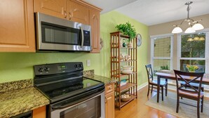 Une cuisine avec des meubles de rangement en bois, un four à micro-ondes en acier inoxydable, une cuisinière noire et un plan de travail en granit.