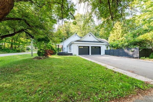 A two-story house with a garage, surrounded by lush greenery and trees.