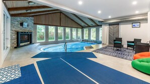 Ein großzügiger Innenbereich mit Swimmingpool, Kamin aus Stein und einer Sitzecke mit Sesseln und einer Couch.