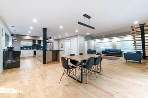 A modern kitchen with a central island, a dining area with a wooden table and chairs, and a living area with a sofa and a TV.