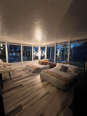 Une chambre avec une grande fenêtre, un lit, une chaise et un plancher en bois.