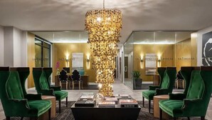 Eine Lobby mit grün gepolsterten Sesseln, einer zentralen Chandelierleuchtre und einem Empfangstresen mit dem Buch 'Barneys'.