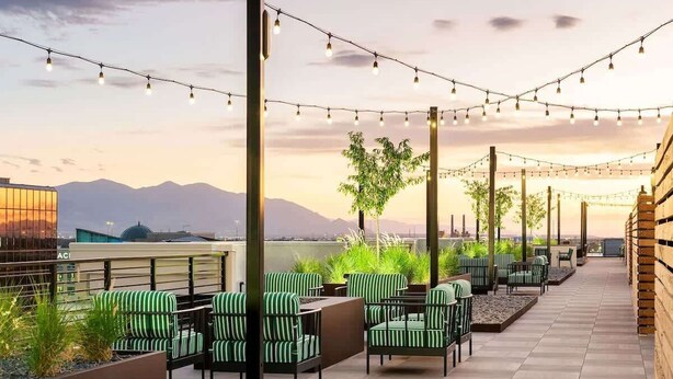 An outdoor seating area with green-striped chairs and tables, string lights overhead, and a view of mountains in the background.