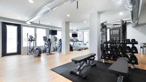 A modern gym with cardio machines, free weights, and a bench.