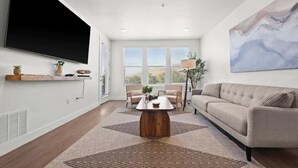 A modern living room with a large flat-screen TV, a beige sofa, a coffee table, and a painting on the wall.
