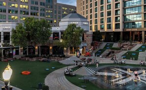 Une cour d’hôtel avec des espaces de repos en plein air, une fontaine et des bâtiments adjacents portant des enseignes.