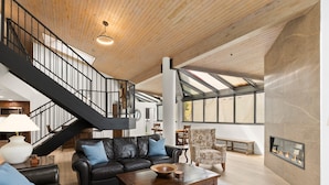 A spacious living area with a black leather sofa, a wooden coffee table, and a patterned armchair. A staircase with a black railing leads to an upper level.