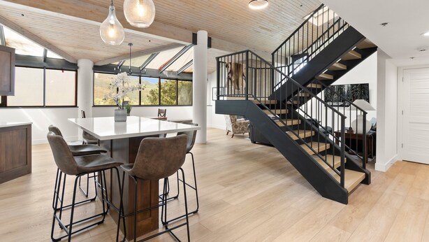 A spacious kitchen with a large island, modern pendant lighting, and a black staircase leading to an upper level.